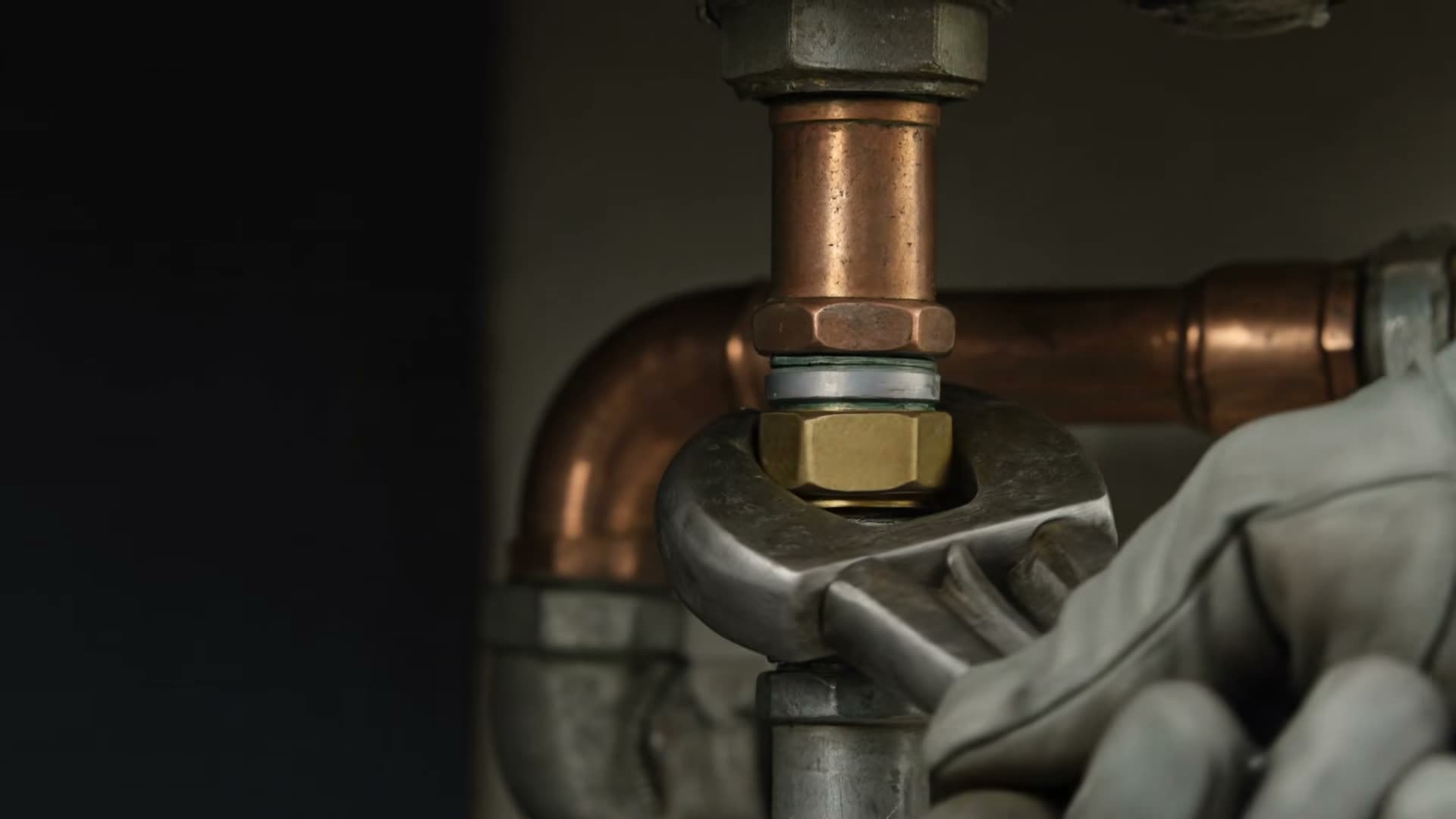 A plumber's gloved hands tightening a brass compression fitting on copper pipe with a wrench.