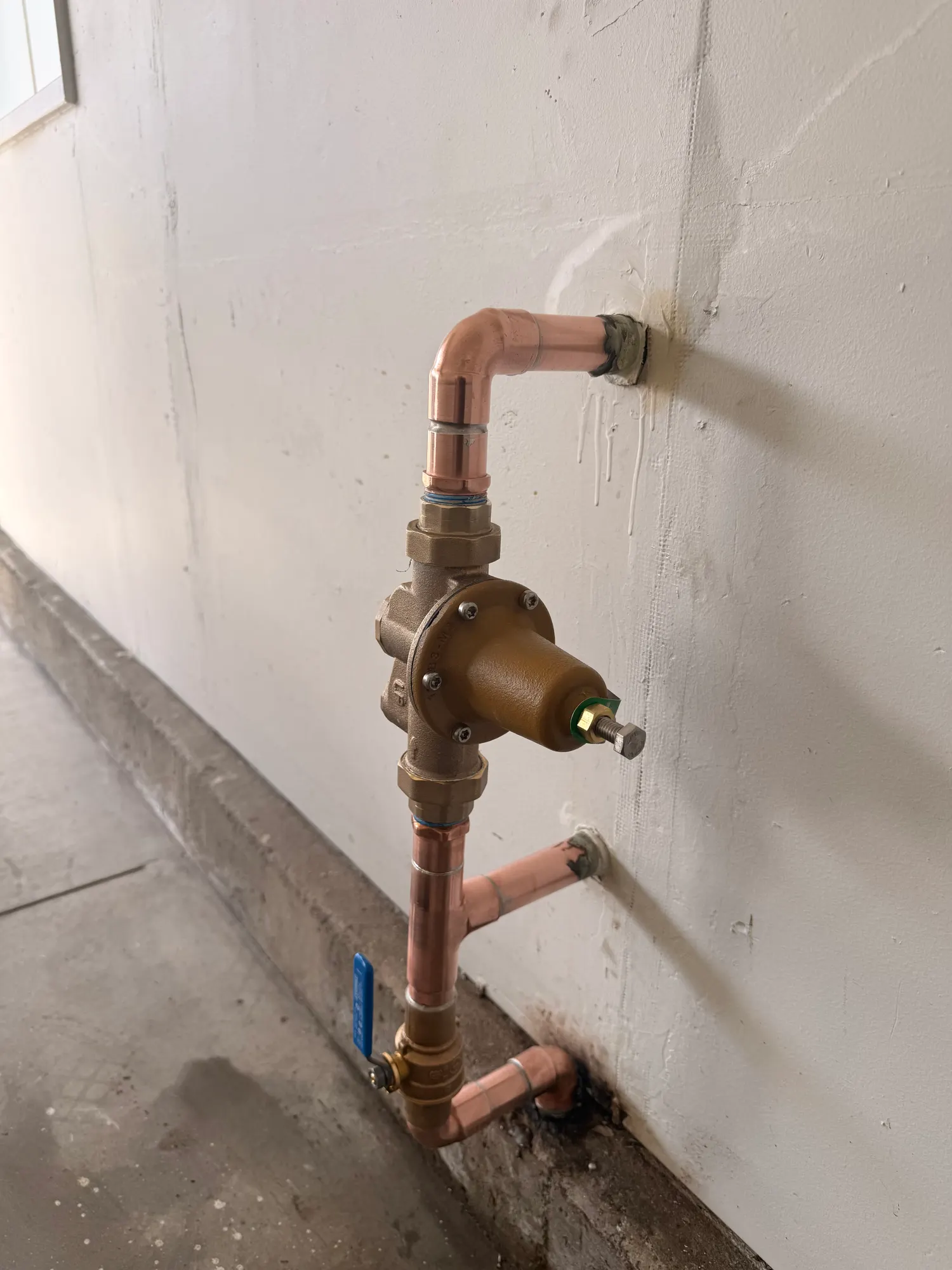 A water supply riser rebuilt in clean copper with a new brass pressure-reducing valve and a new shutoff valve at the base of a wall.