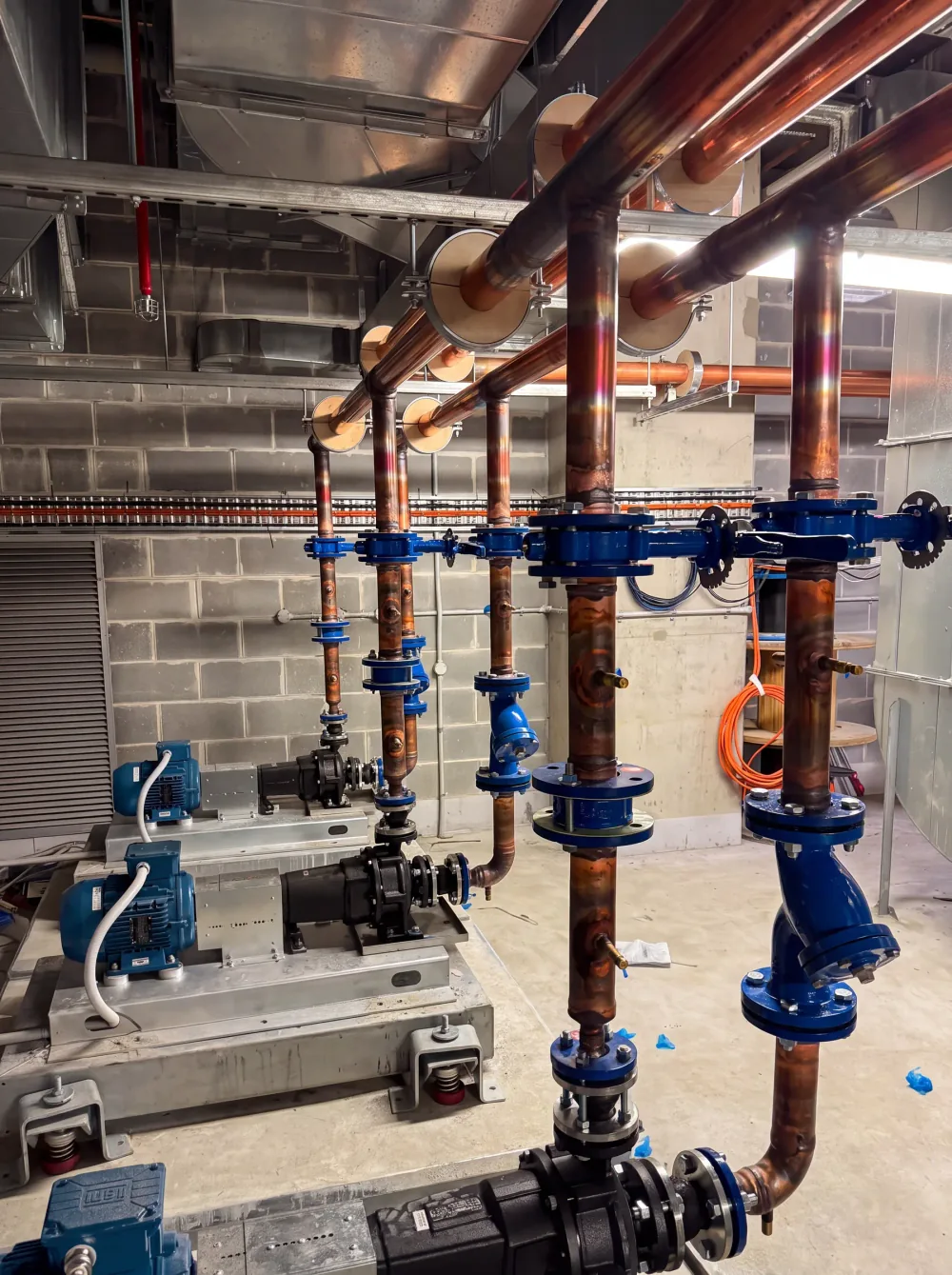 A commercial plant room: large-diameter copper risers running to flanged isolation valves above a pump set.