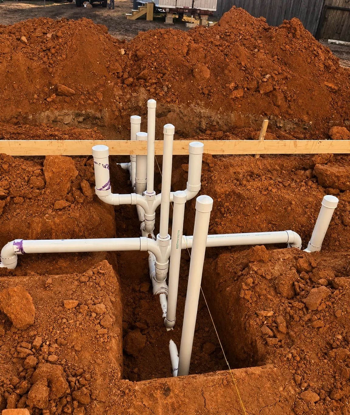Underground drain, waste and vent (DWV) work: white PVC piping in an open excavated trench.